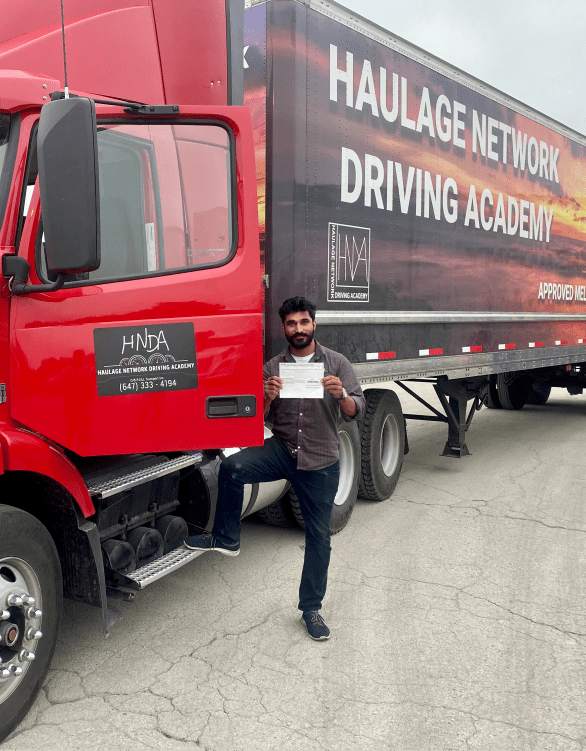 student standing next to a truck, holding a commercial driver's license